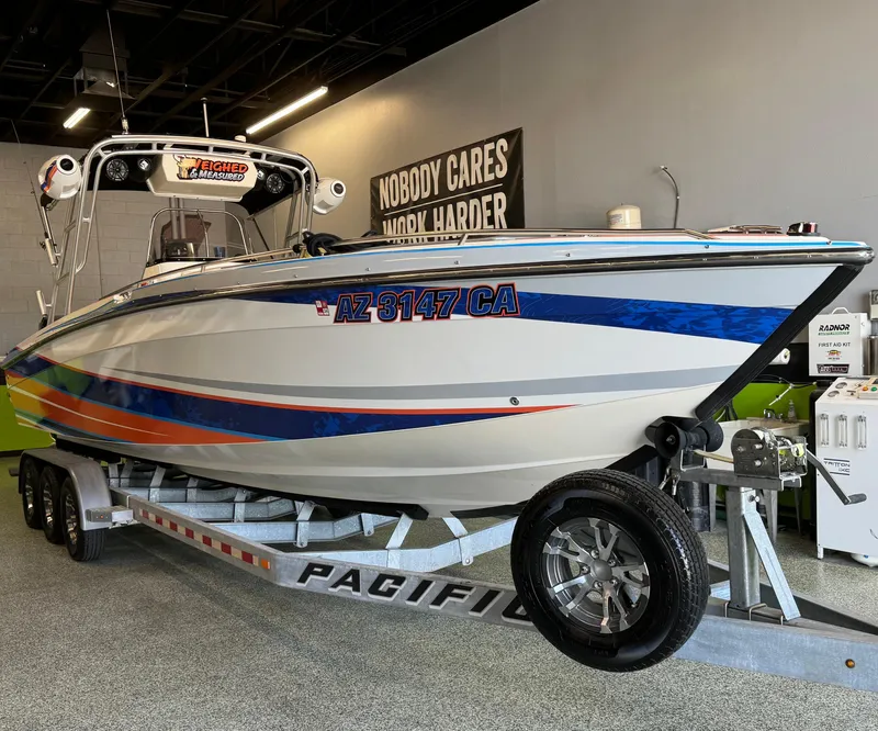 Slide: The Image of 1999 Wellcraft Scarab 302 boat on trailer, vibrant blue and orange design, indoor showroom. - 2