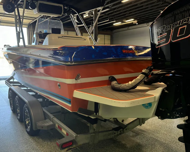 Slide: The Image of 1999 Wellcraft Scarab 302 boat on trailer in garage, vibrant orange and blue design. - 6
