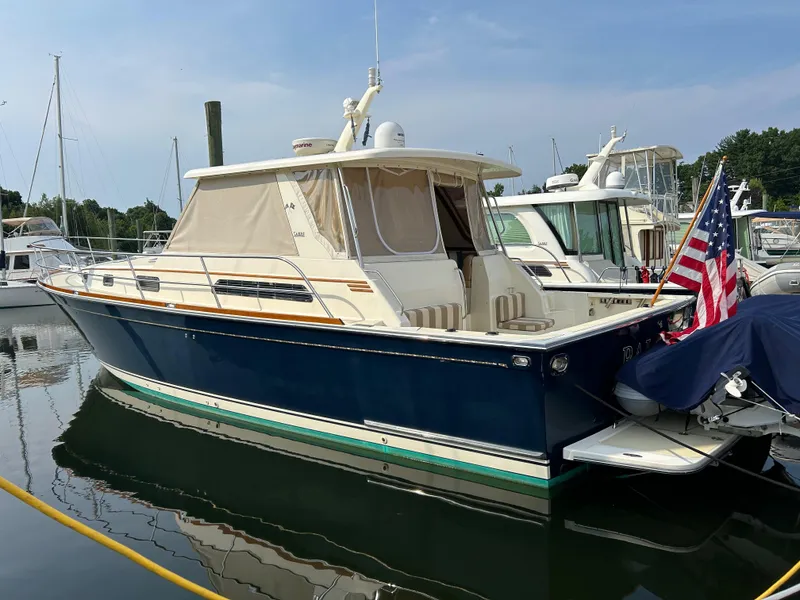 The Image of 2009 Sabre Hardtop Express boat docked with American flag, blue hull, and beige canopy. - 0