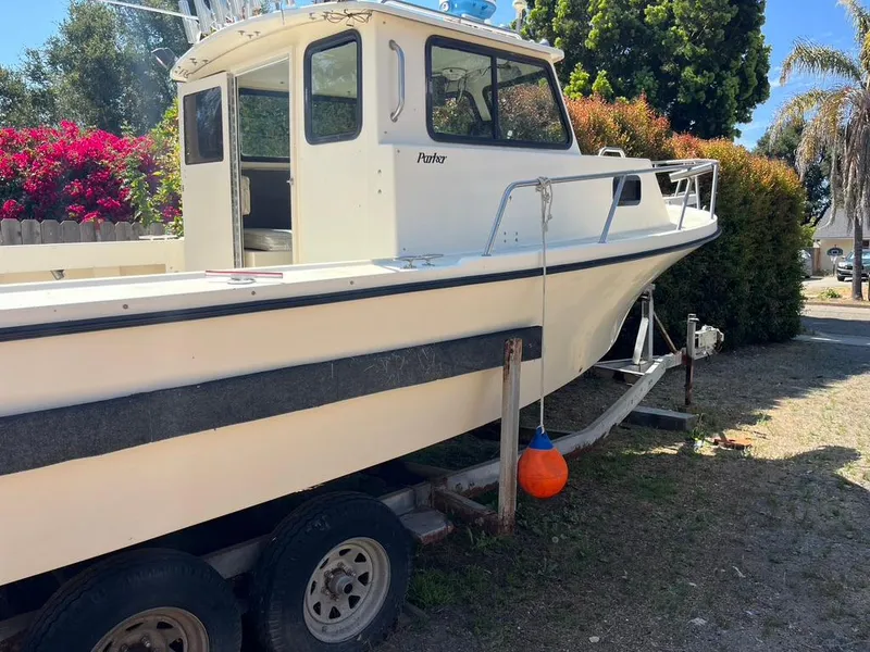Slide: The Image of 1994 Parker 2520 boat on trailer, surrounded by trees and flowers. - 2