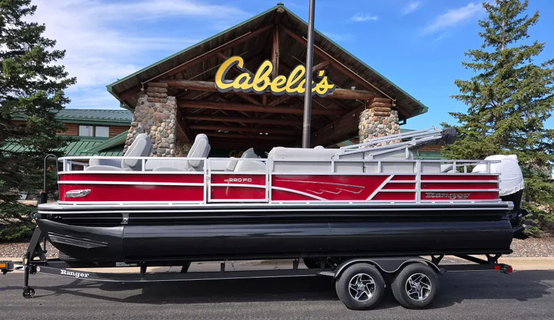 The Image of 2024 Ranger Reata 200C pontoon boat on trailer outside Cabela's store. - 0