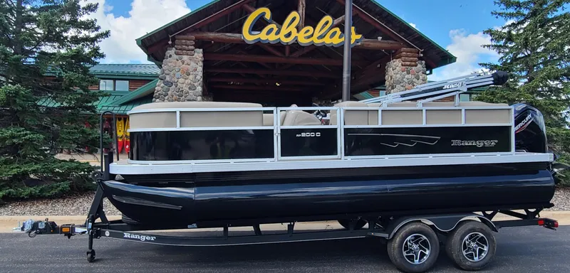 The Image of 2024 Ranger Reata 200C pontoon boat on trailer outside Cabela's store. - 0