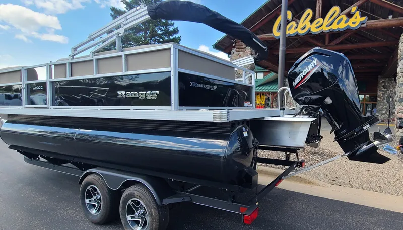 Slide: The Image of 2024 Ranger Reata 200C pontoon boat on trailer outside Cabela's store. - 2