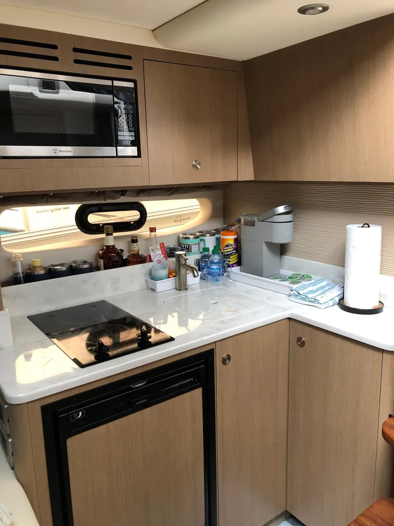 Slide: The Image of Compact kitchen in 2018 Sea Ray 350 Sundancer Coupe with modern appliances and wooden cabinetry. - 16