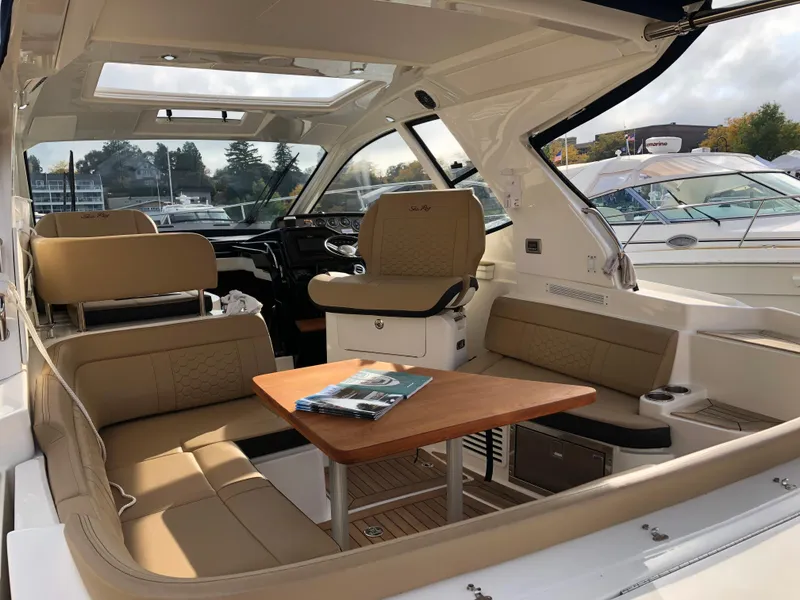 Slide: The Image of 2018 Sea Ray 350 Sundancer Coupe interior with beige seating and wooden table. - 2