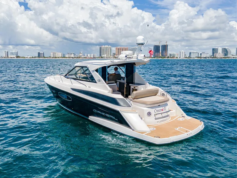 Slide: The Image of 2015 Regal 42 Sport Coupe yacht cruising on open water with city skyline backdrop. - 23