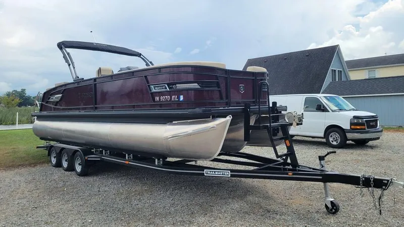 Slide: The Image of 2023 AquaPatio 275 CBE iMPACT pontoon boat on trailer, parked outdoors. - 2