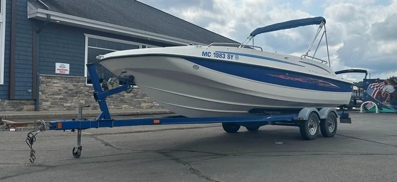Slide: The Image of 2006 Bayliner 217 boat on trailer, parked outside a building under cloudy skies. - 1