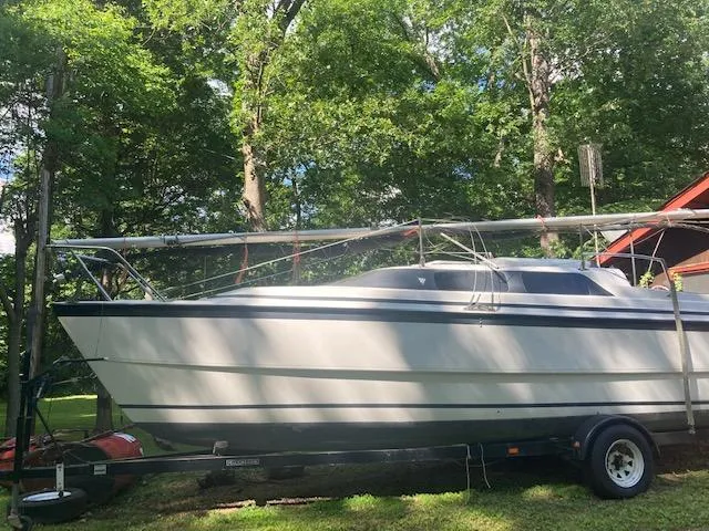 The Image of 1997 MacGregor 26 X sailboat on trailer, surrounded by lush green trees. - 1