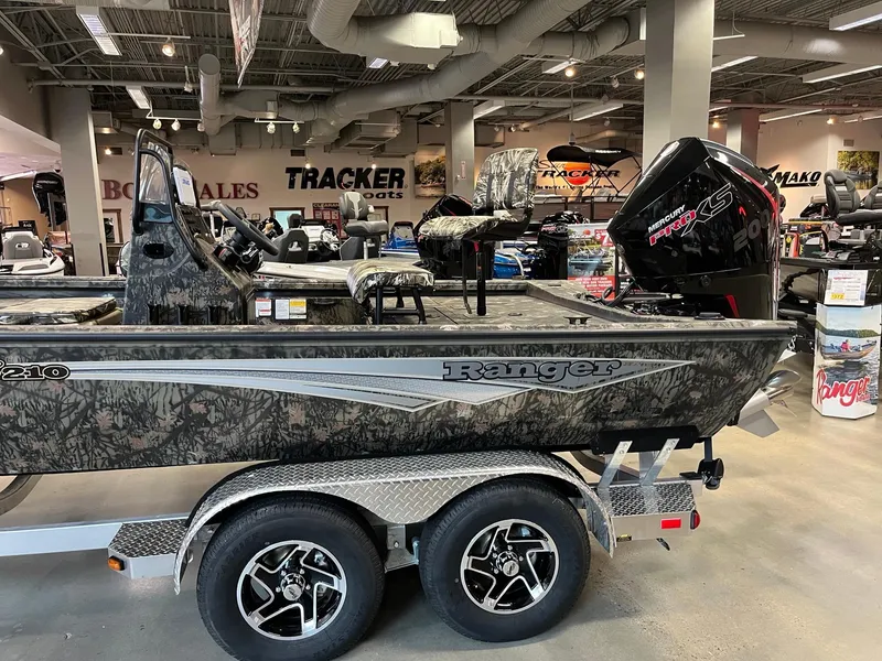 Slide: The Image of 2024 Ranger RB210 boat in showroom, camo design, dual-axle trailer, powerful outboard motor. - 4