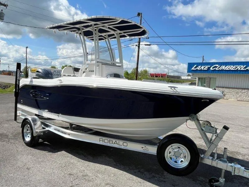 Slide: The Image of 2024 Robalo R180 boat on trailer, parked outdoors under a blue sky. - 19