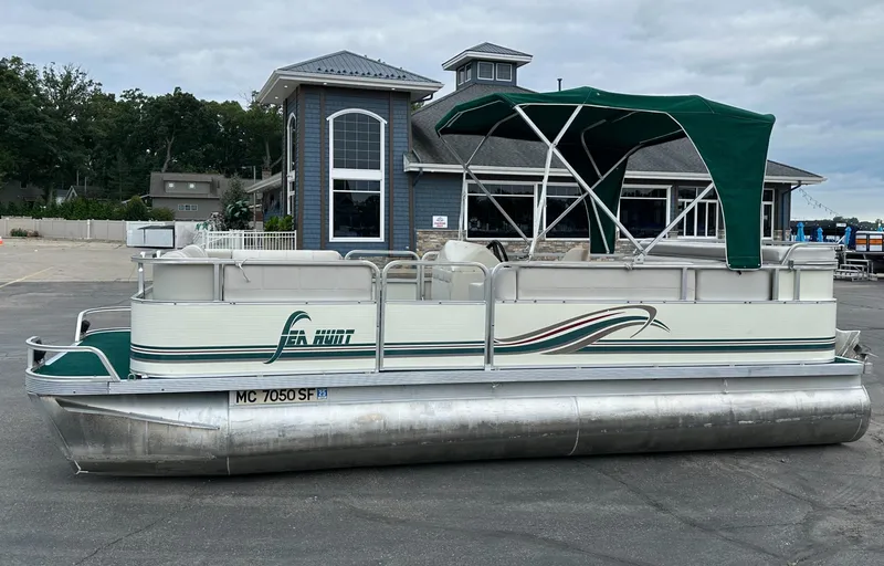 Slide: The Image of 2001 Sea Hunt 20 pontoon boat with green canopy, parked near a building. - 2