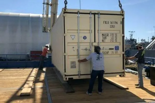 Slide: The Image of Crane lifting AlumaCat 100 container, 2000 model, onto a wooden platform with workers assisting. - 22