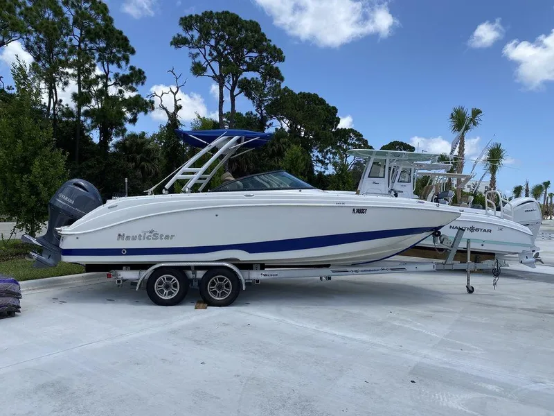 Slide: The Image of 2019 NauticStar 243 DC boat on trailer, parked outdoors under blue sky. - 0