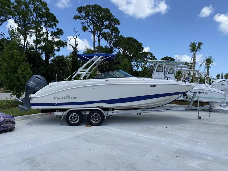 Slide: The Image of 2019 NauticStar 243 DC boat on trailer, parked outdoors under blue sky. - 11