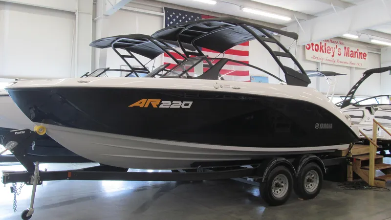 Slide: The Image of 2024 Yamaha Boats AR220 on trailer in showroom with American flag backdrop. - 0