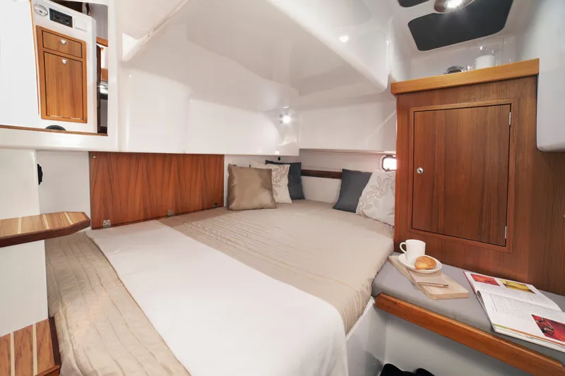 Slide: The Image of 2024 Sargo 31 cabin interior with cozy bed, wooden accents, and reading materials. - 12
