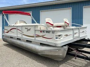 Slide: The Image of 2006 Crest Super Sport pontoon boat with red canopy, parked near blue building. - 3