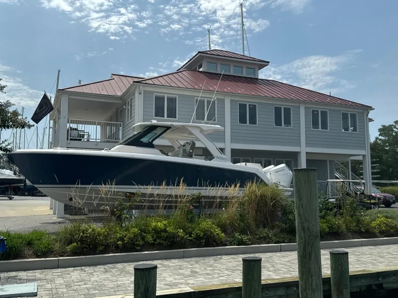 Slide: The Image of 2025 Tiara Yachts 34 LS docked near a modern marina building. - 2
