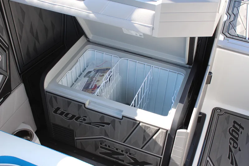 Slide: The Image of 2024 Tigé Ultré 25ZX boat cooler with open lid and storage compartments. - 14
