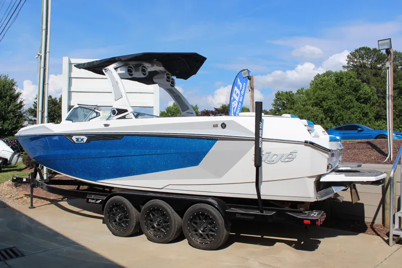 Slide: The Image of 2024 Tigé Ultré 25ZX boat on trailer, blue and white design, parked outdoors. - 3