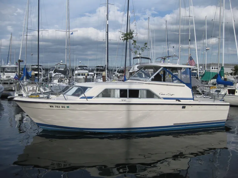 The Image of 1977 Chris-Craft 28' Cruiser docked in a marina, surrounded by sailboats. - 0