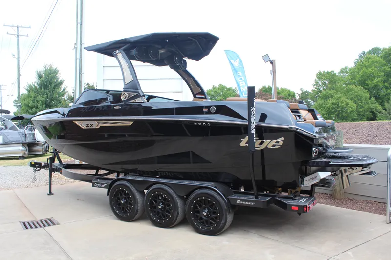 Slide: The Image of 2024 Tigé Ultré 23ZX boat on trailer, sleek black design, parked outdoors. - 2