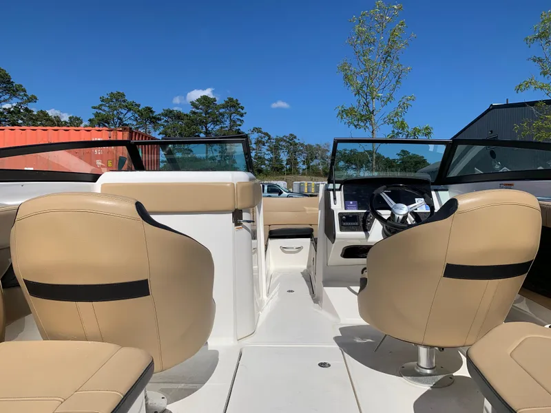 Slide: The Image of 2022 Sea Ray SPX 230 OB boat interior with beige seating and steering wheel, under clear blue sky. - 4