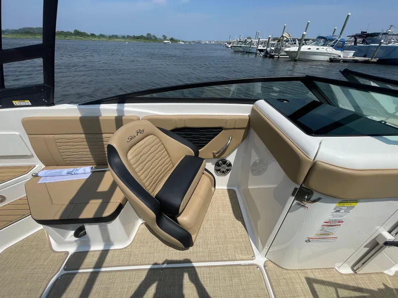 Slide: The Image of 2023 Sea Ray SPX 230 Outboard interior with tan seating, docked by the water. - 17