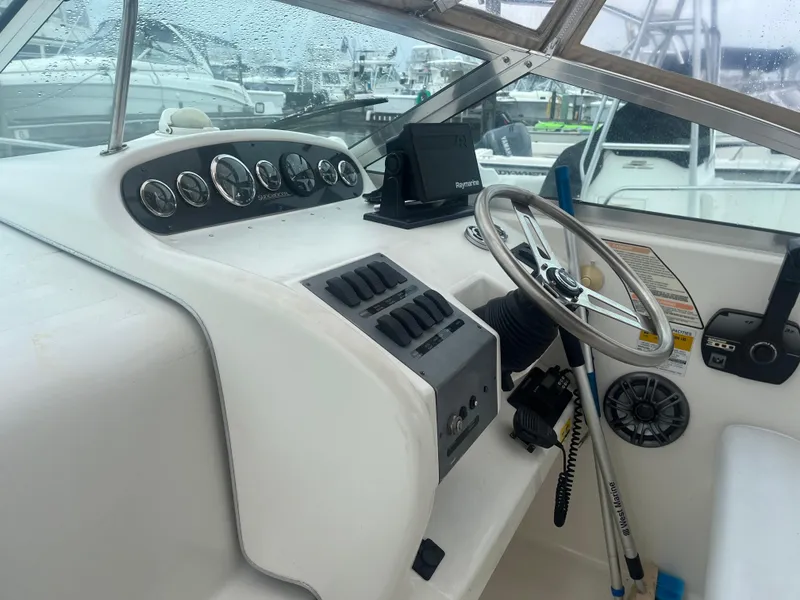 Slide: The Image of 1995 Sea Ray 250 Sundancer helm with gauges and steering wheel in marina setting. - 32