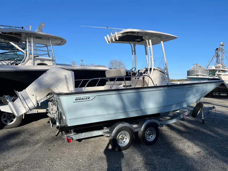 Slide: The Image of 2025 Boston Whaler 210 Montauk boat on trailer, parked outdoors under clear blue sky. - 19