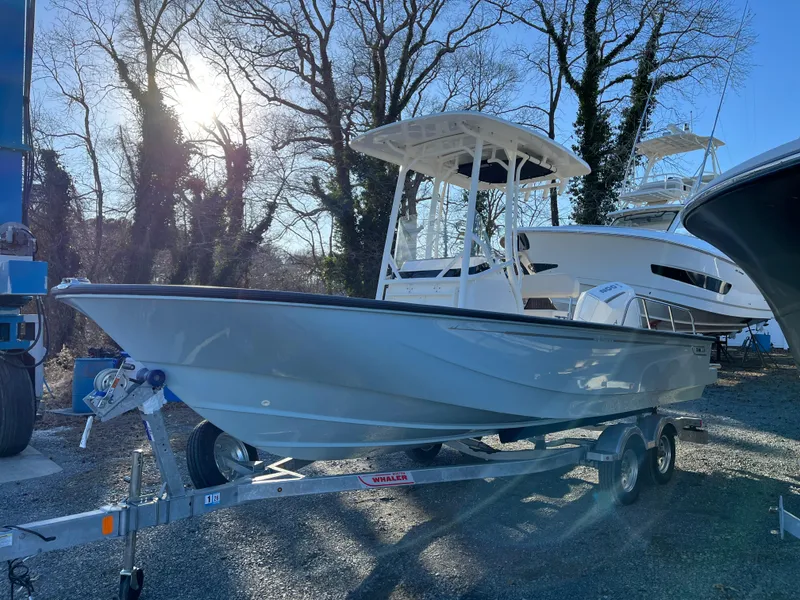 Slide: The Image of 2025 Boston Whaler 210 Montauk boat on trailer, parked outdoors with trees in background. - 20