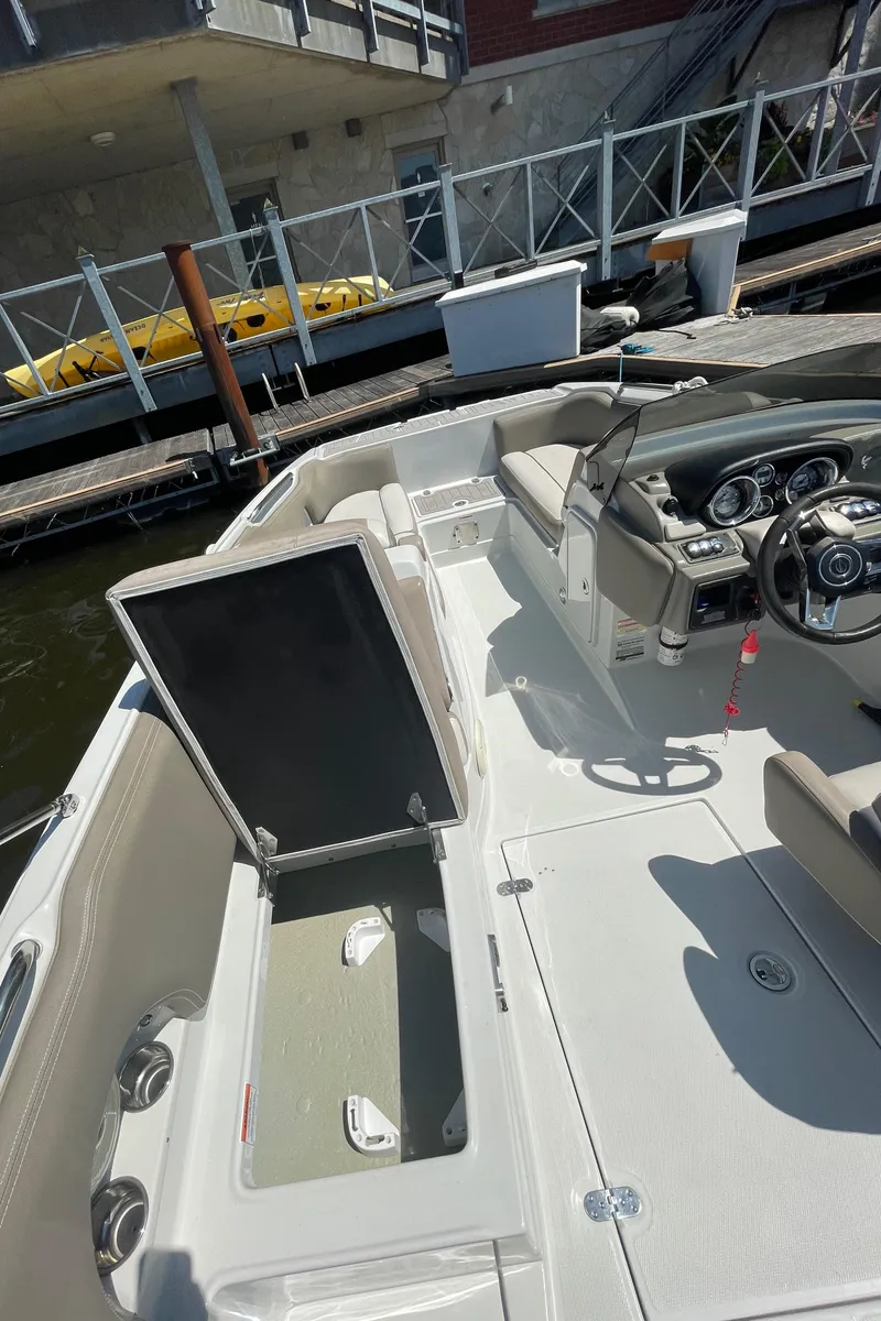 Slide: The Image of 2020 Crownline E 205 XS boat interior with open storage compartment, docked by the water. - 19