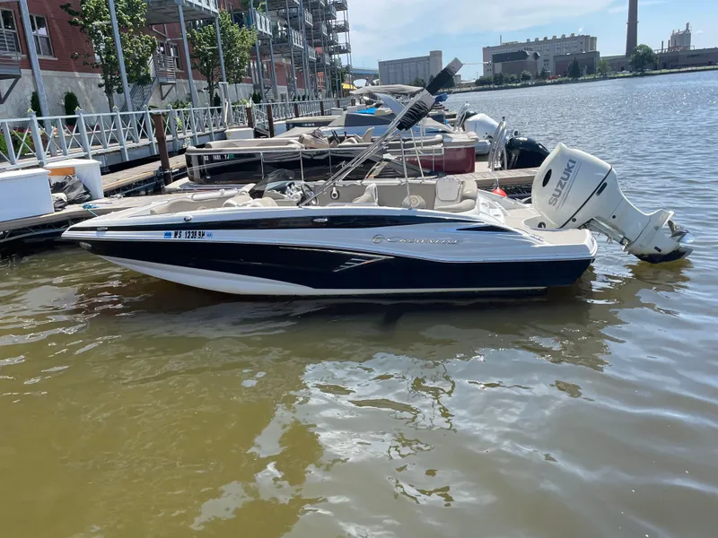 Slide: The Image of 2020 Crownline E 205 XS boat docked on a sunny waterfront. - 2