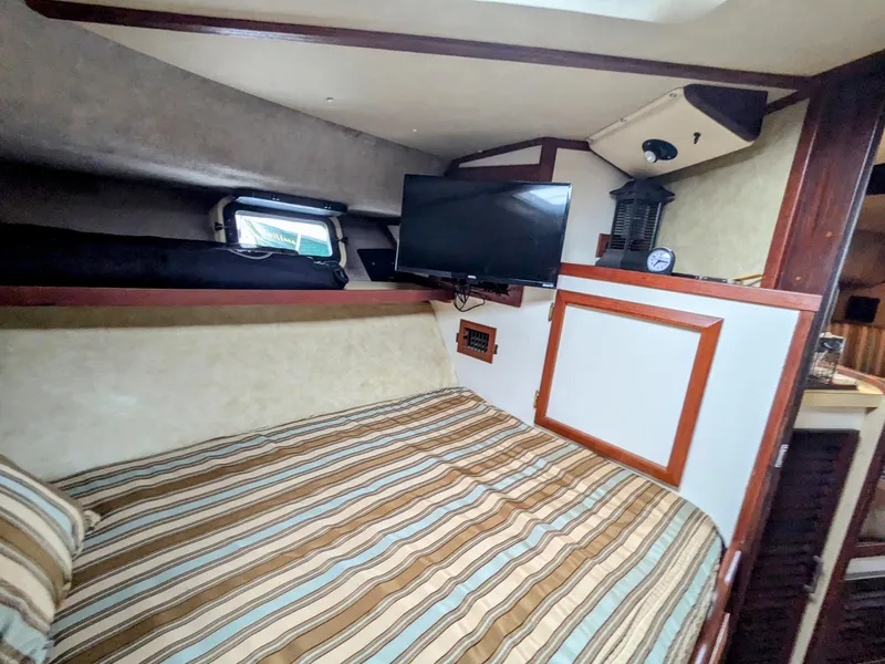 Slide: The Image of 1981 Silverton 37 Convertible cabin with striped bedding and mounted TV. - 29