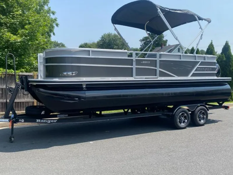 Slide: The Image of 2024 Ranger Reata 223C pontoon boat on trailer, parked outdoors. - 0