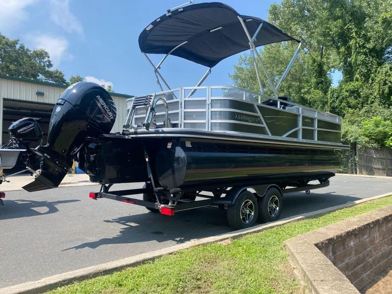 Slide: The Image of 2024 Ranger Reata 223C pontoon boat with canopy on trailer, parked outdoors. - 1
