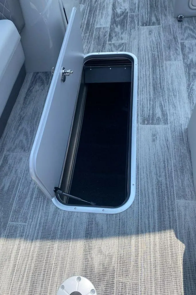 Slide: The Image of 2024 Ranger Reata 223C boat storage compartment with open hatch on wood-patterned floor. - 13
