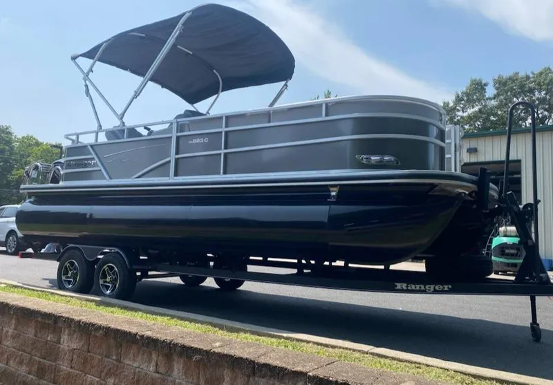 Slide: The Image of 2024 Ranger Reata 223C pontoon boat on trailer, parked outdoors. - 2