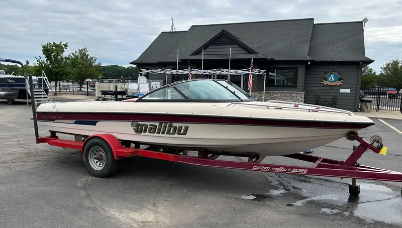 The Image of 2000 Malibu Response LXi boat on a red trailer, parked near a building. - 0