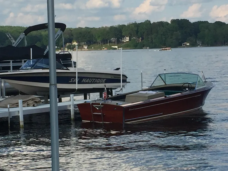 Slide: The Image of 1966 Century Resorter boat docked on a serene lake with lush green surroundings. - 7