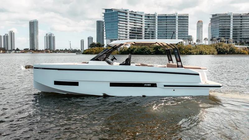 Slide: The Image of 2025 De Antonio Yachts D32 OPEN cruising on water with city skyline backdrop. - 5