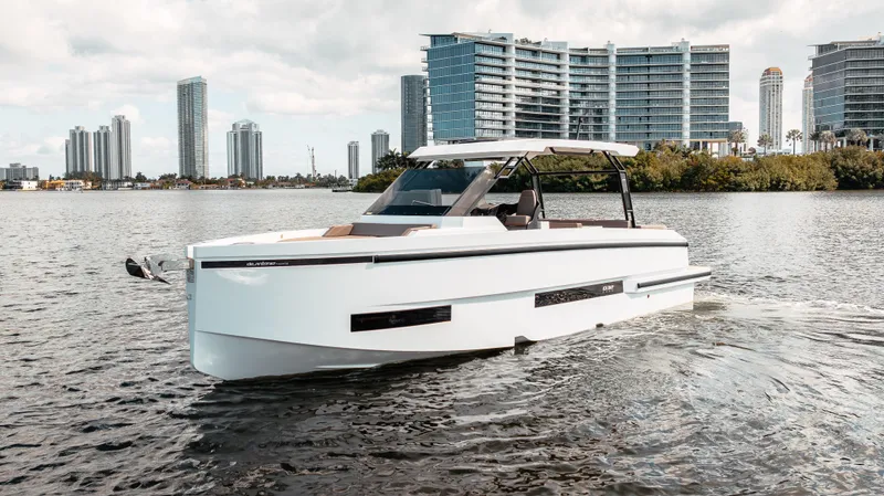 Slide: The Image of 2025 De Antonio Yachts D32 OPEN cruising on a scenic waterfront with modern buildings. - 6