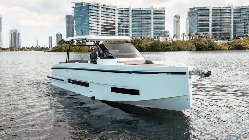Slide: The Image of 2025 De Antonio Yachts D32 OPEN cruising on water with modern buildings in the background. - 8