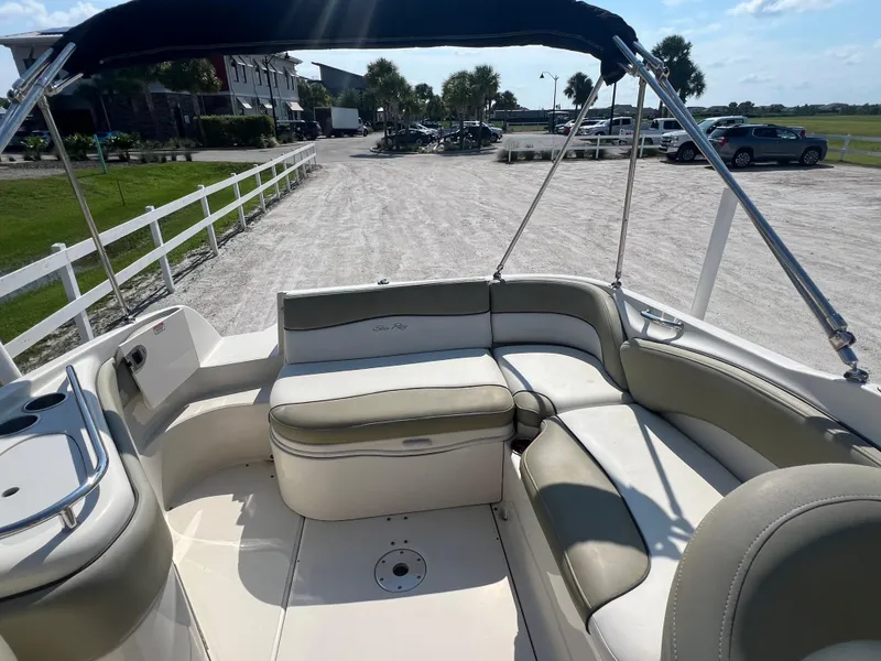 Slide: The Image of 2006 Sea Ray 240 Sundeck interior with beige seating and canopy, parked on gravel. - 13