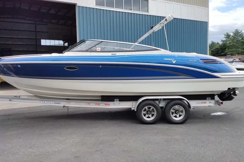 Slide: The Image of 2016 Formula 270 Bowrider boat on trailer, blue and white, parked outside a warehouse. - 9