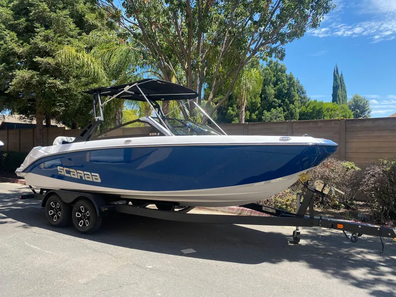 The Image of 2025 Scarab 235 SE boat on trailer, blue and white design, parked outdoors. - 0