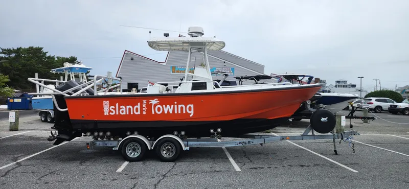 The Image of 2000 Boston Whaler Justice 24 boat on trailer, labeled "Island Towing," parked in a lot. - 0