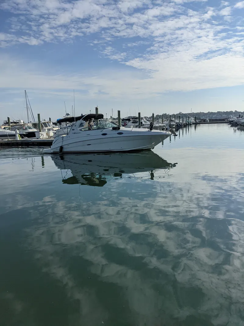 Slide: The Image of 2005 Sea Ray 280 Sundancer boat docked in a serene marina under a partly cloudy sky. - 1
