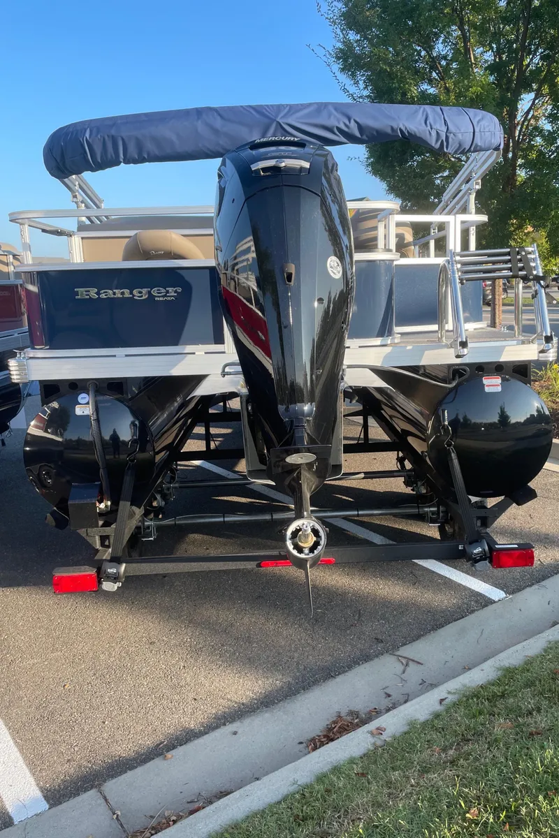 Slide: The Image of 2024 Ranger Reata 200F pontoon boat with outboard motor, parked on pavement. - 6